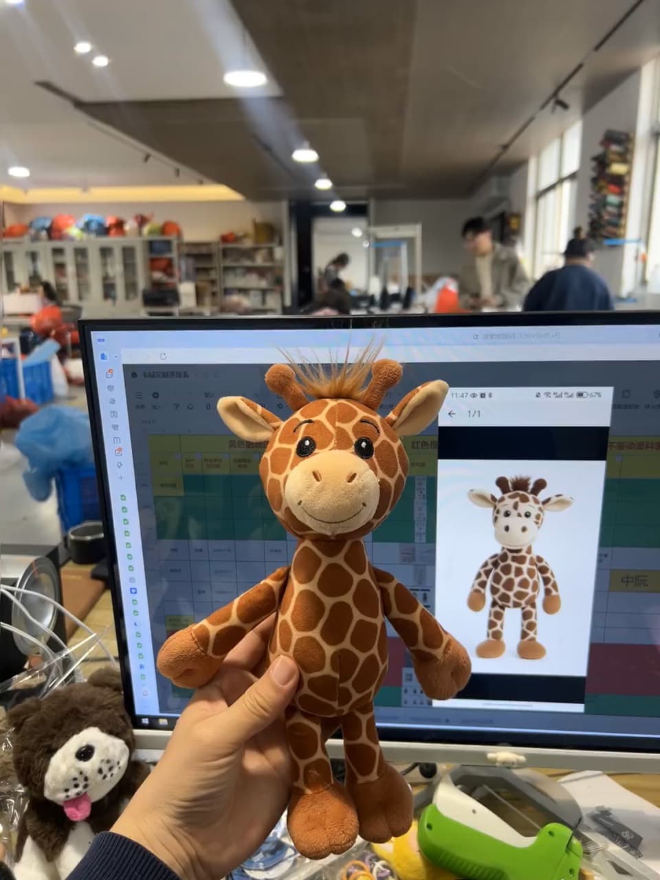 Custom giraffe plush sample beside its design reference on the factory floor